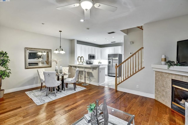 dining room featuring a tile fireplace, ceiling fan with notable chandelier, and light hardwood / wood-style floors