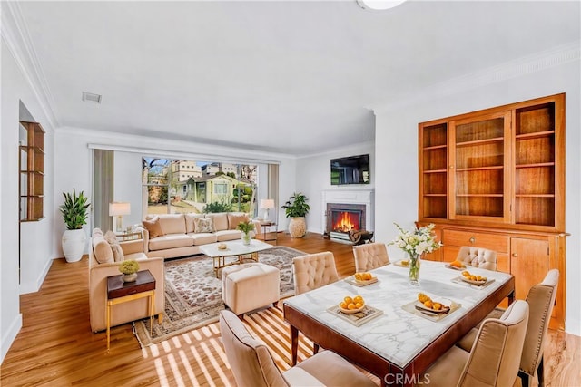 dining room with built in shelves, ornamental molding, and light hardwood / wood-style flooring