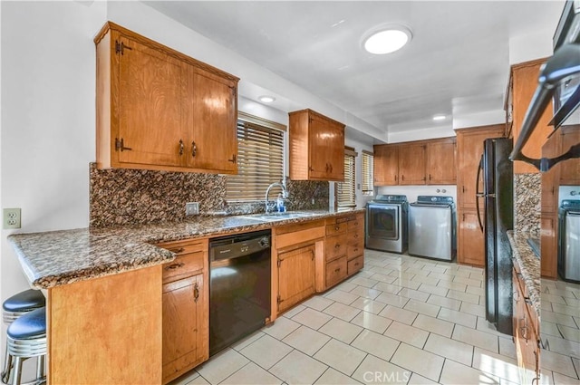 kitchen with black appliances, washer and dryer, backsplash, dark stone counters, and sink