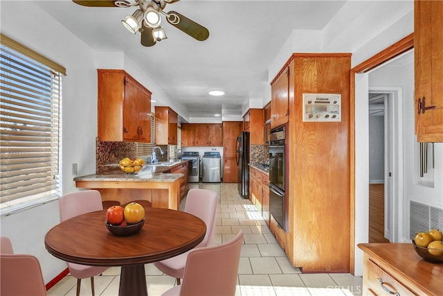 kitchen featuring independent washer and dryer, black appliances, kitchen peninsula, light tile patterned floors, and backsplash