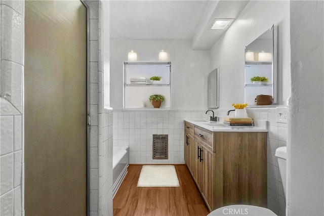 bathroom with tile walls, a tub to relax in, wood-type flooring, and vanity