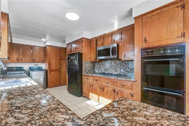 kitchen featuring washing machine and dryer, black appliances, tasteful backsplash, dark stone counters, and sink