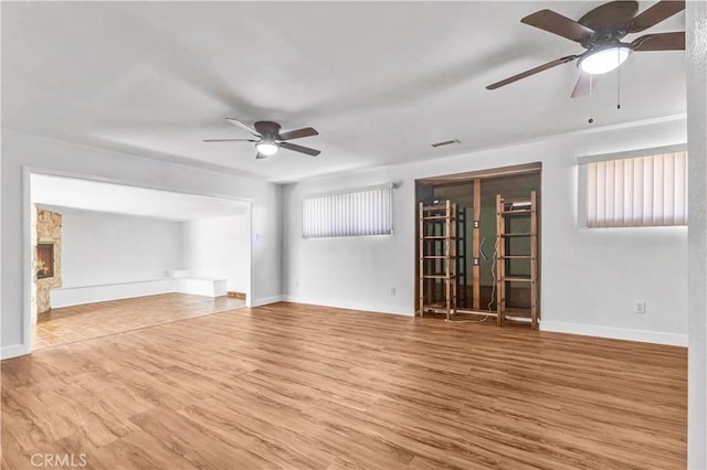 unfurnished room with hardwood / wood-style flooring, ceiling fan, and a stone fireplace