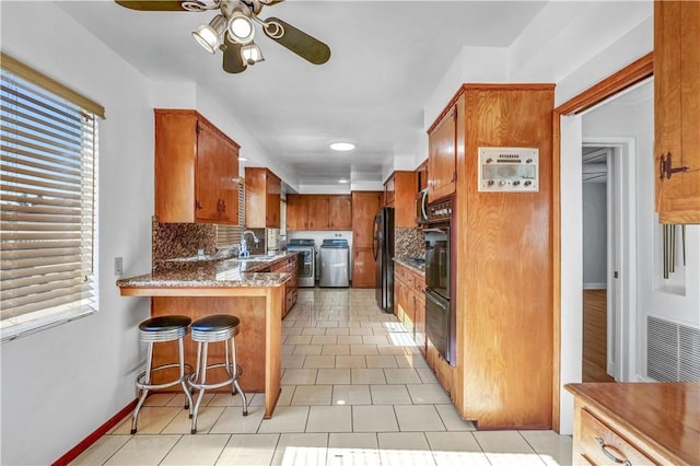 kitchen featuring kitchen peninsula, light tile patterned floors, decorative backsplash, washer and dryer, and a kitchen breakfast bar