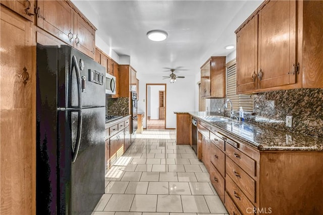 kitchen with dark stone countertops, black appliances, light tile patterned floors, sink, and tasteful backsplash