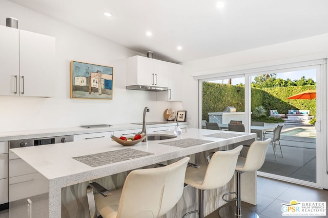 kitchen featuring white cabinets, a kitchen breakfast bar, an island with sink, and light tile patterned floors