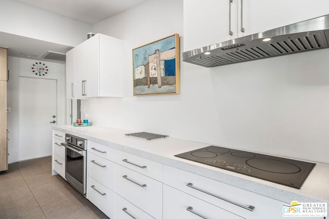 kitchen with stainless steel oven, exhaust hood, light tile patterned floors, black electric cooktop, and white cabinetry