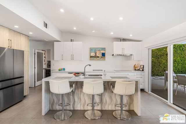 kitchen with sink, white cabinetry, stainless steel refrigerator, and an island with sink