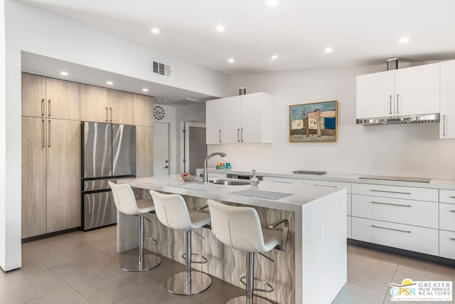 kitchen featuring stainless steel refrigerator, a kitchen island with sink, white cabinetry, and sink