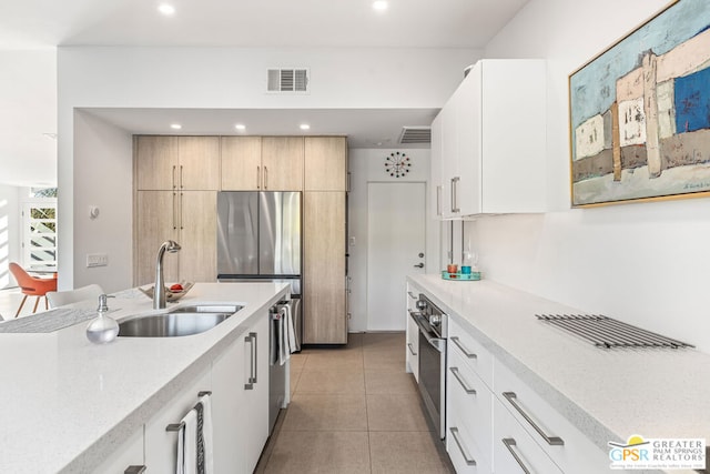 kitchen featuring white cabinets, stainless steel appliances, light brown cabinetry, sink, and light tile patterned flooring