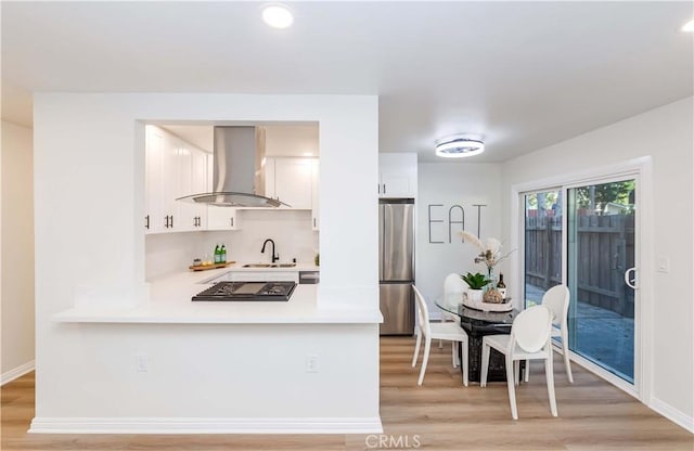 kitchen featuring sink, white cabinetry, light hardwood / wood-style flooring, stainless steel appliances, and range hood