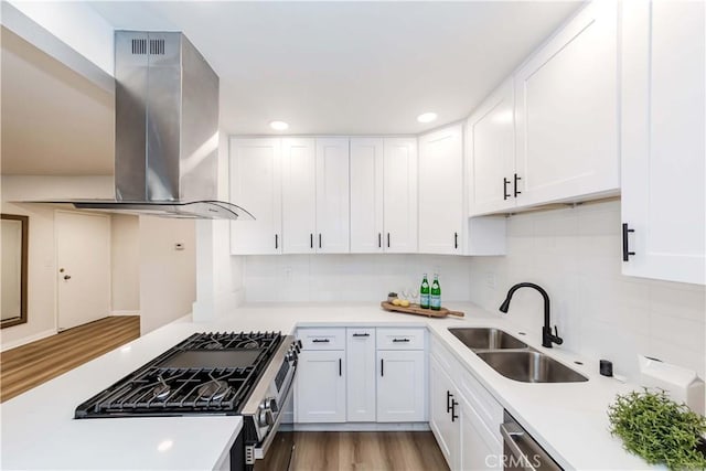 kitchen with sink, stainless steel gas range oven, white cabinetry, tasteful backsplash, and island range hood