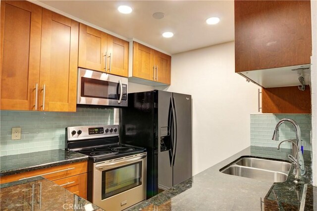 kitchen with stainless steel appliances, dark stone counters, decorative backsplash, and sink