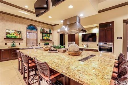 kitchen with stainless steel oven, island exhaust hood, crown molding, and a kitchen breakfast bar