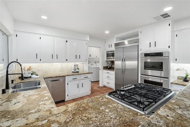 kitchen featuring built in appliances, light tile patterned floors, sink, white cabinetry, and washing machine and clothes dryer