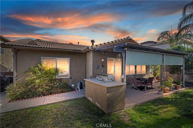 back house at dusk with a patio, an outdoor kitchen, and a yard