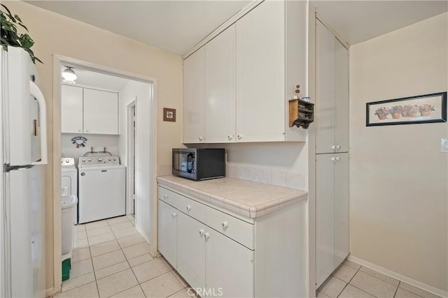 kitchen featuring white fridge, washing machine and dryer, light tile patterned floors, tile countertops, and white cabinetry