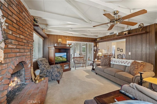 living room with vaulted ceiling with beams, ceiling fan, a brick fireplace, wood walls, and light colored carpet