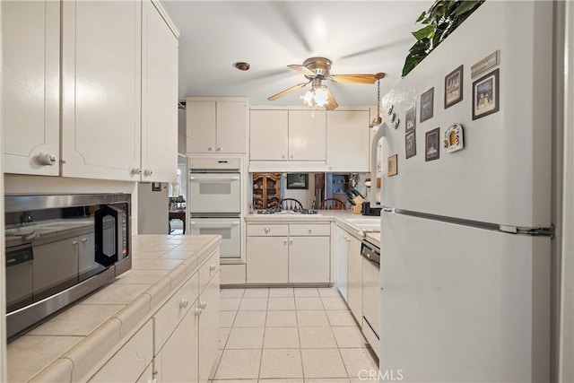 kitchen featuring stainless steel appliances, white cabinetry, tile countertops, light tile patterned flooring, and ceiling fan