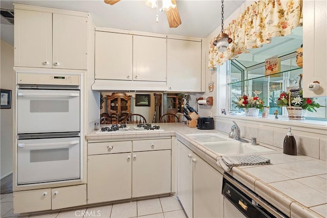 kitchen with white appliances, tile countertops, light tile patterned floors, white cabinets, and sink