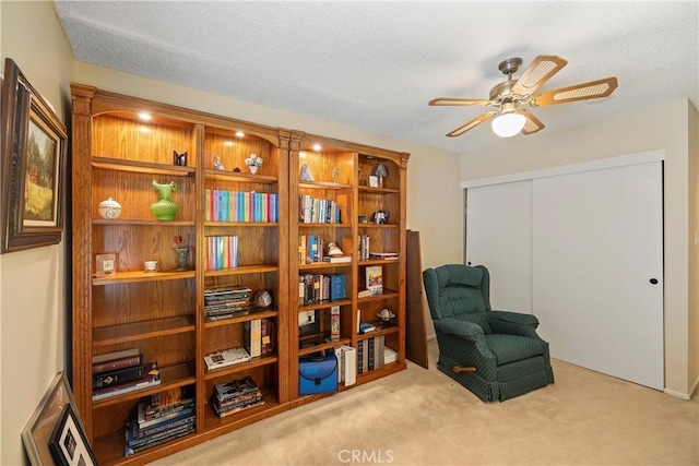 living area with light colored carpet, ceiling fan, and a textured ceiling