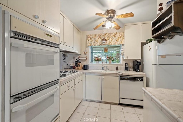 kitchen with white appliances, tile counters, light tile patterned floors, ceiling fan, and sink