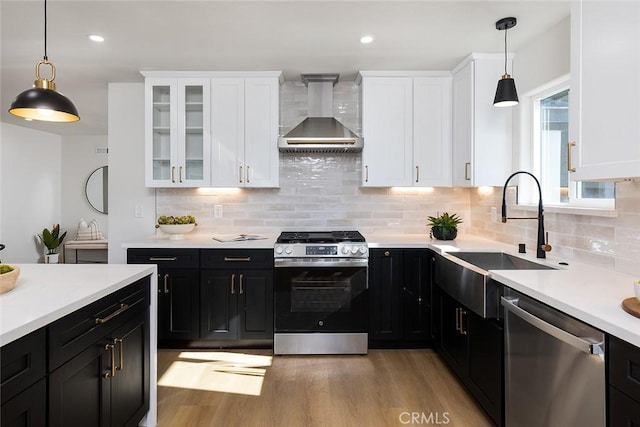 kitchen featuring stainless steel appliances, sink, wall chimney exhaust hood, decorative backsplash, and hanging light fixtures