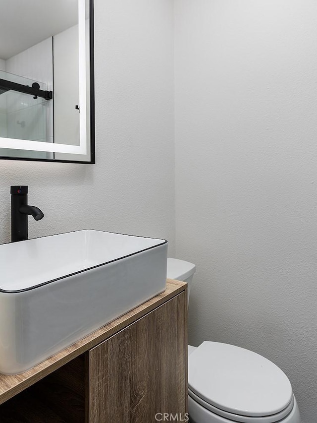 bathroom featuring toilet, a shower with door, and vanity