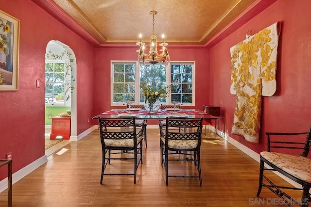 dining area with an inviting chandelier, hardwood / wood-style flooring, and a tray ceiling