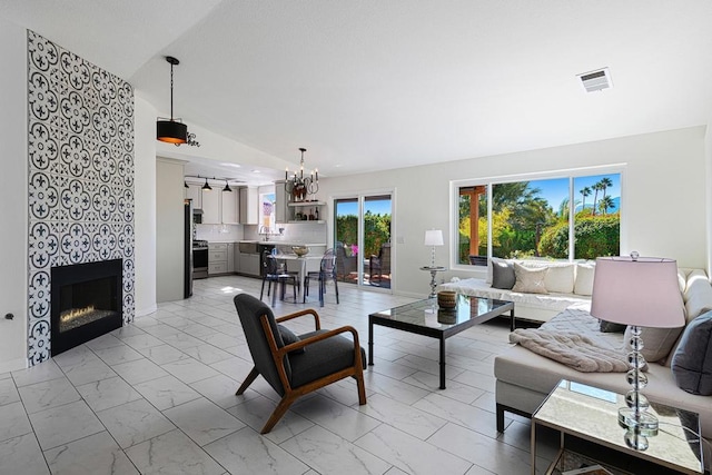 living room featuring lofted ceiling, a tiled fireplace, sink, and a notable chandelier