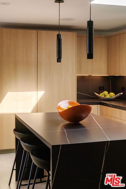 kitchen with backsplash, a kitchen bar, pendant lighting, and light brown cabinets