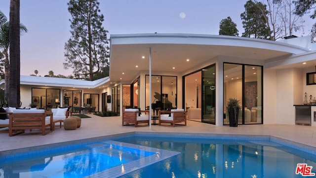 pool at dusk with an outdoor hangout area, a patio, and an in ground hot tub