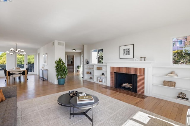 living room featuring a brick fireplace, light wood-type flooring, a notable chandelier, and plenty of natural light