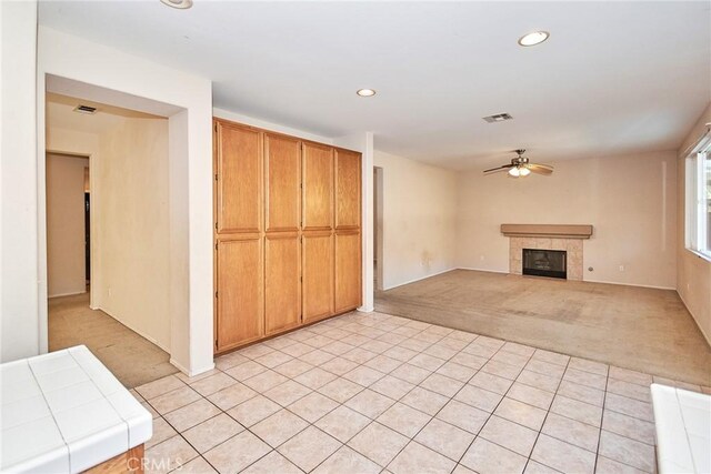 kitchen with ceiling fan, a tiled fireplace, tile countertops, and light carpet