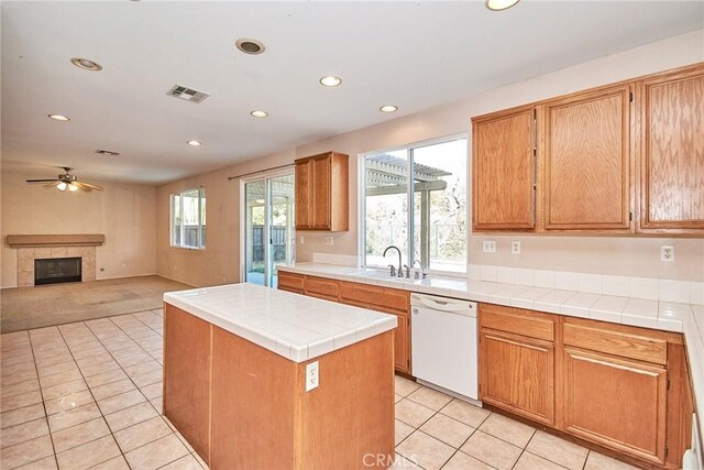 kitchen with sink, a tile fireplace, dishwasher, tile counters, and a kitchen island