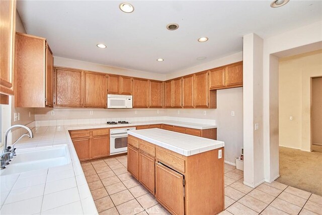 kitchen with sink, a center island, light tile patterned flooring, white appliances, and tile counters