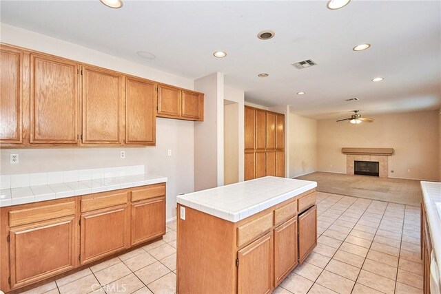 kitchen with tile countertops, a center island, light tile patterned floors, a tiled fireplace, and ceiling fan