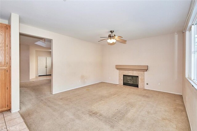 unfurnished living room featuring a tile fireplace, light carpet, and ceiling fan