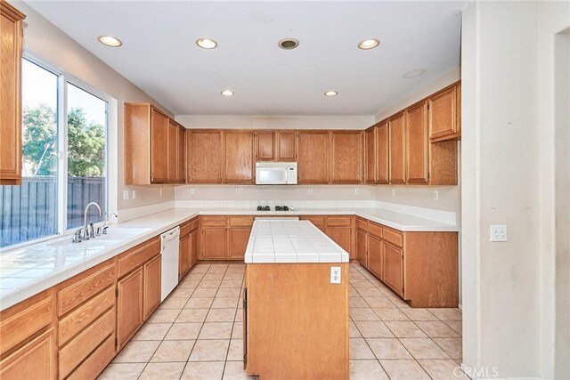 kitchen featuring white appliances, a center island, light tile patterned floors, tile countertops, and sink