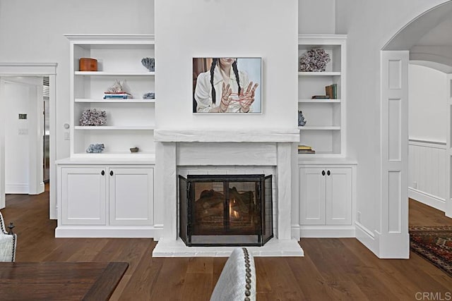 living room with dark wood-type flooring, built in features, and a fireplace