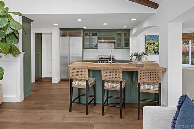 kitchen with wooden counters, a breakfast bar area, stainless steel built in refrigerator, green cabinets, and backsplash