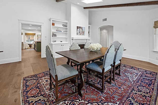 dining area featuring built in features, a skylight, beamed ceiling, and hardwood / wood-style floors