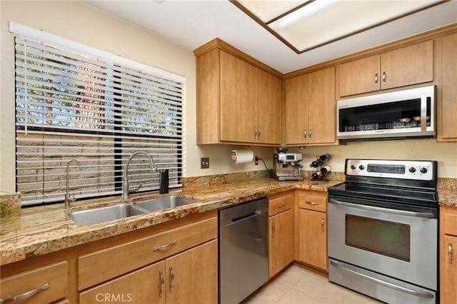 kitchen with sink, stainless steel appliances, light stone counters, and light tile patterned floors