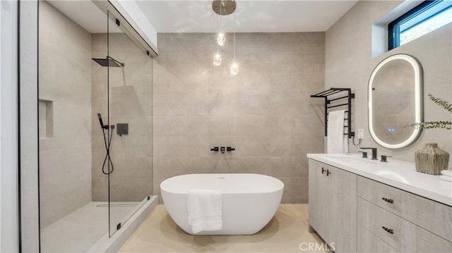 bathroom with separate shower and tub, vanity, and tile walls