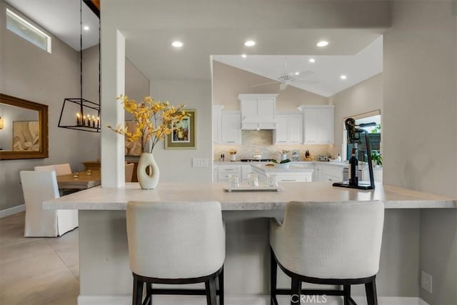 kitchen with tasteful backsplash, kitchen peninsula, white cabinets, and a kitchen breakfast bar