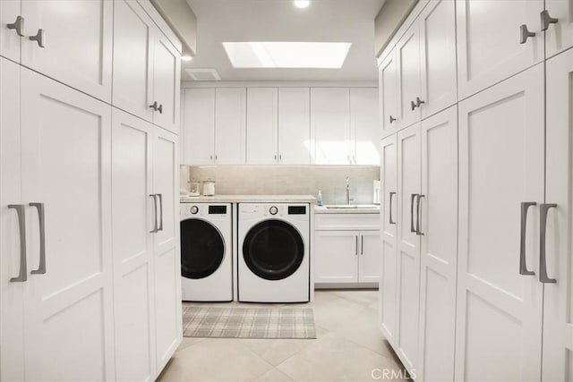 laundry area featuring sink, cabinets, light tile patterned floors, a skylight, and washing machine and dryer