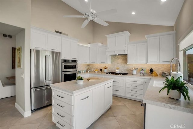 kitchen featuring stainless steel appliances, a center island, white cabinetry, backsplash, and high vaulted ceiling