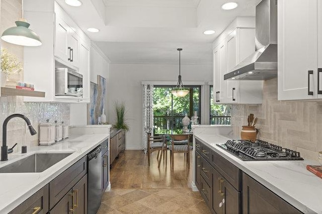 kitchen featuring white cabinetry, appliances with stainless steel finishes, wall chimney exhaust hood, light stone counters, and sink