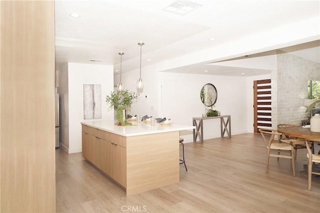 kitchen with light brown cabinets, a breakfast bar, hanging light fixtures, and light hardwood / wood-style flooring