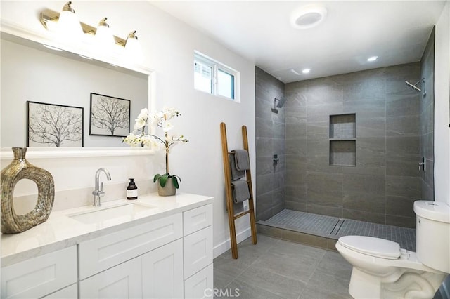 bathroom with toilet, a tile shower, and vanity